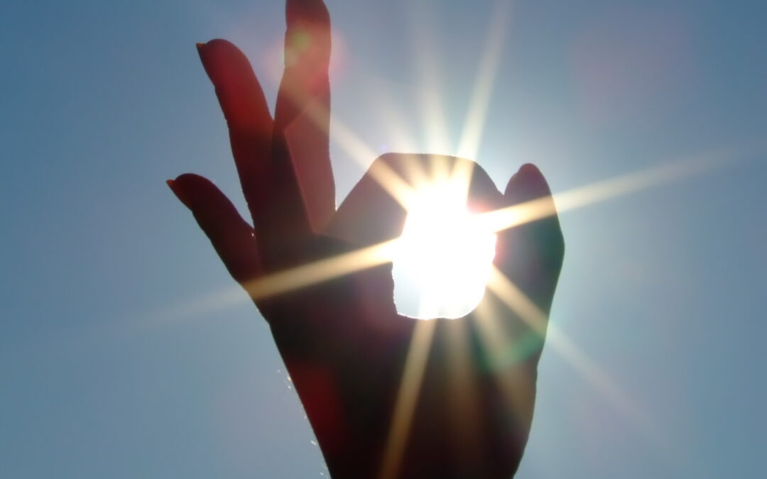 Silhouette of a female hand, the blue sky and the bright sun